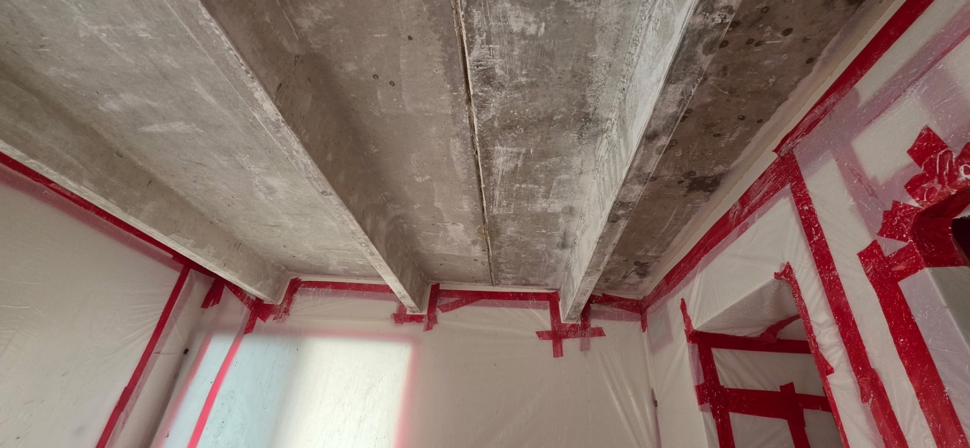 Concrete ceiling deck during asbestos popcorn ceiling abatement in a Cheesman Park high-rise, with red tape and plastic containment near downtown Denver